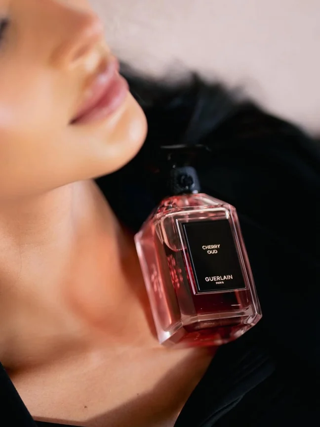 Guerlain bottle close-up against skin and black feather outfit